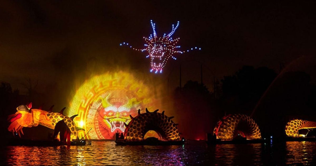 Verlichte drakeninstallatie op het water 's nachts, met een droneshow in de vorm van een draak in de lucht