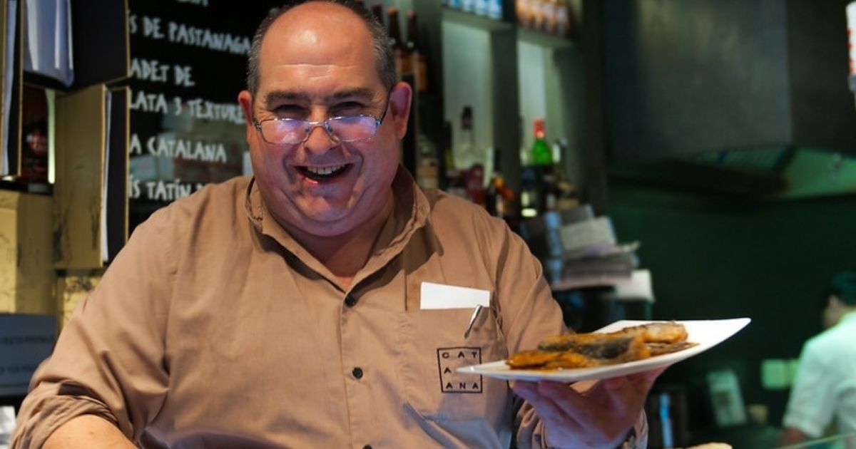 Lachende medewerker van restaurant Catalana met een bord gerecht in zijn hand