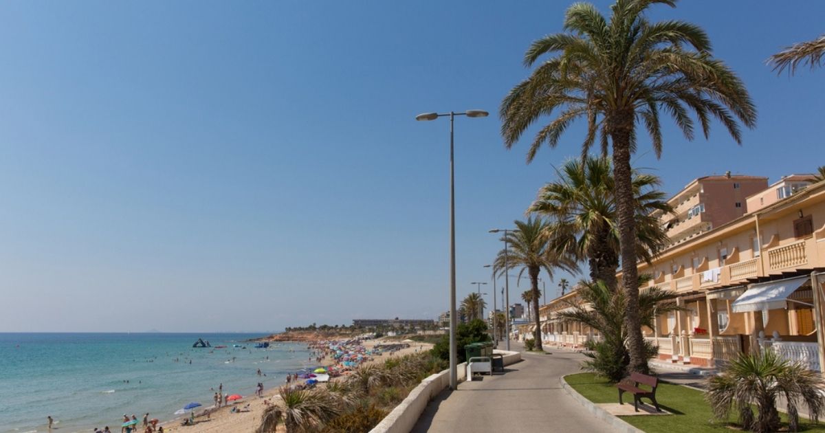 Boulevard langs een druk strand met palmbomen, appartementen en turquoise zee op een zonnige dag