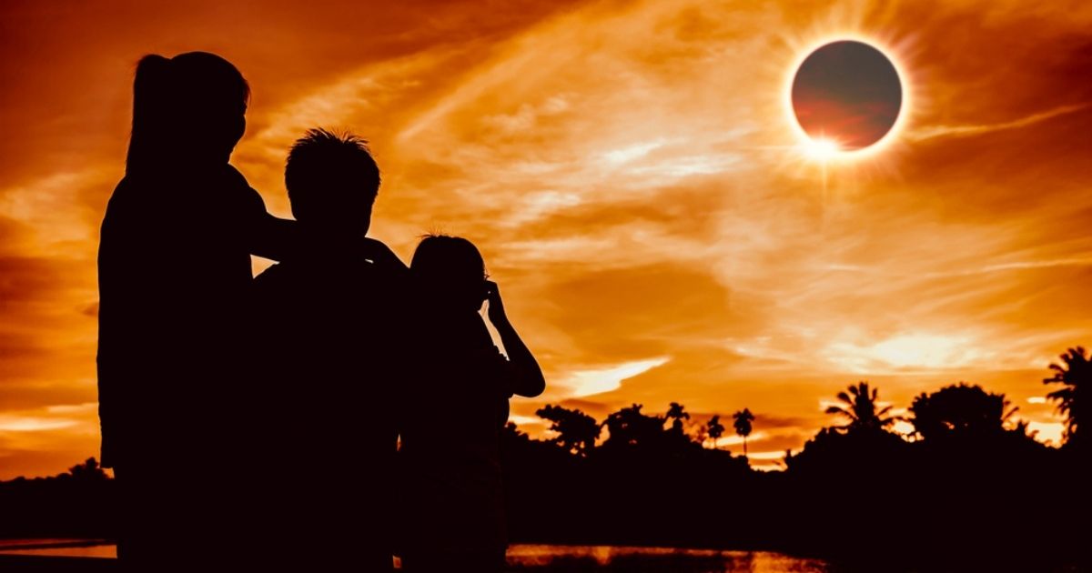 Silhouet van een gezin dat naar een totale zonsverduistering kijkt tegen een oranje gekleurde hemel