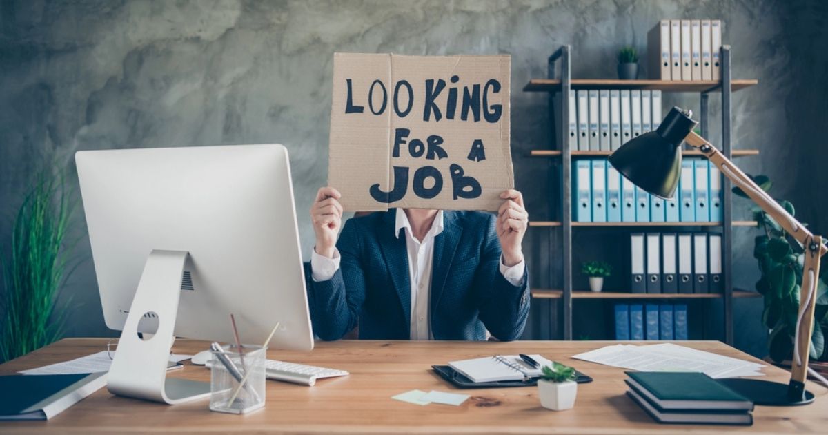 Persoon aan bureau houdt kartonnen bord voor gezicht met de tekst "Looking for a job