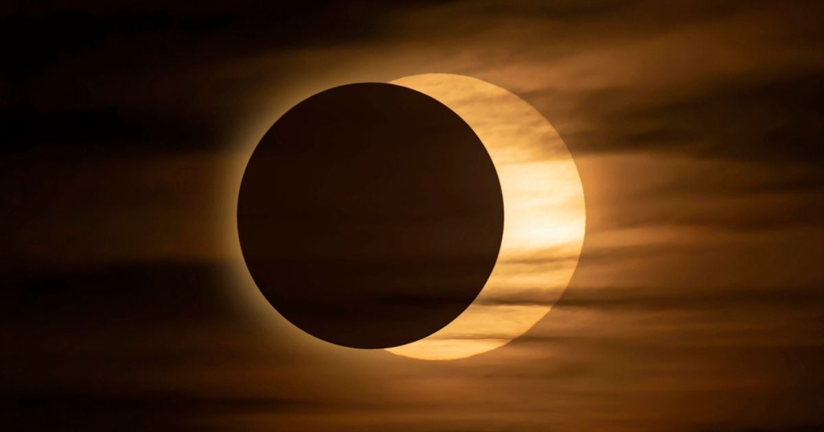 Gedeeltelijke zonsverduistering waarbij de maan de zon grotendeels bedekt, omgeven door een gouden gloed tegen bewolkte lucht
